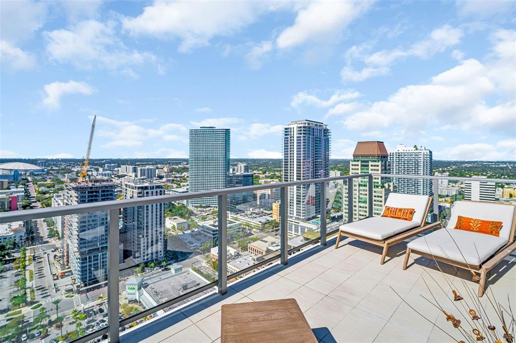 A high-rise balcony features two lounge chairs overlooking a city skyline with several skyscrapers — 301 1ST STREET S UNIT 3305, ST PETERSBURG, FL