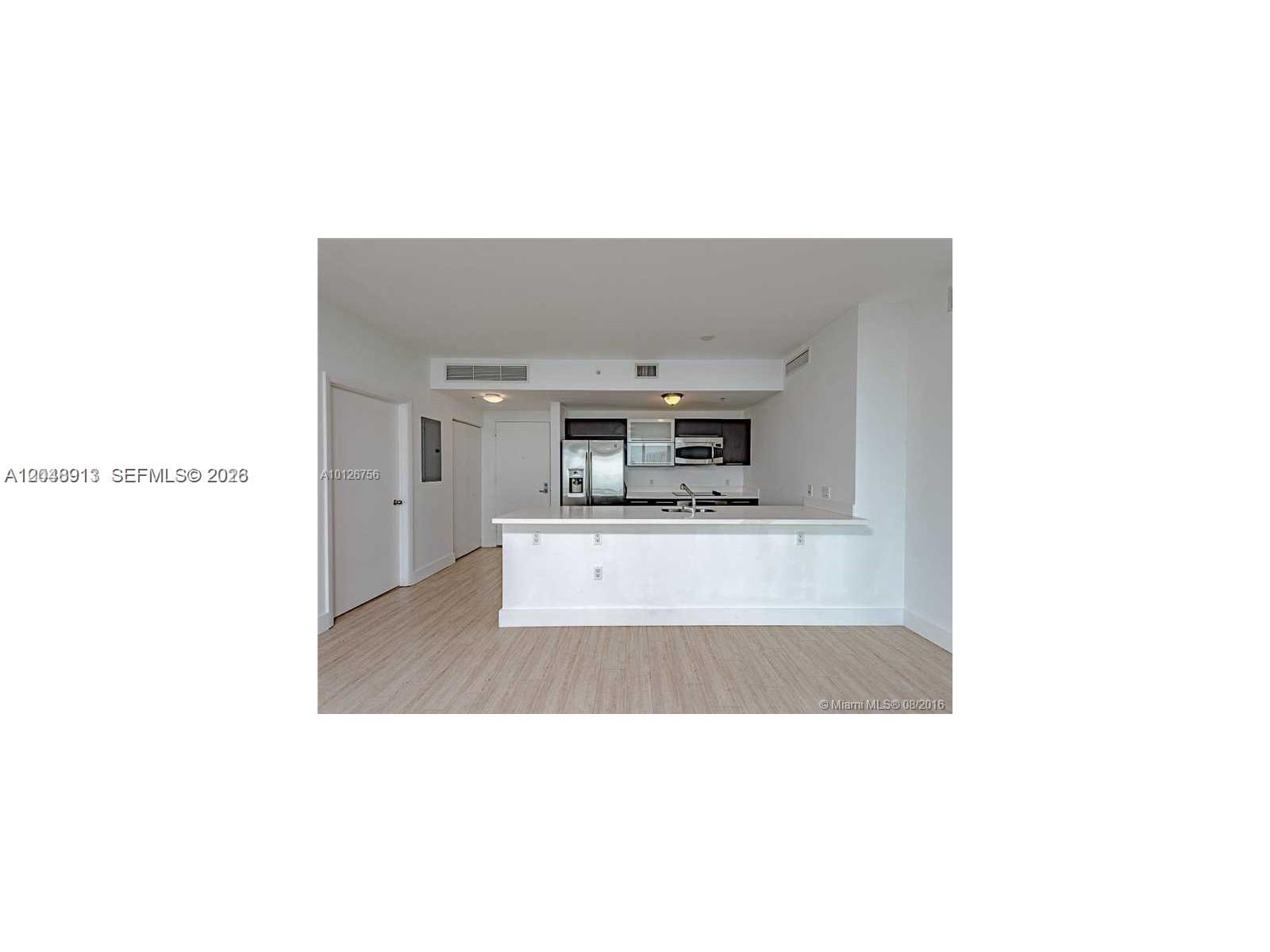 An open-concept kitchen features a white breakfast bar, stainless steel appliances, and light wood flooring — 90 SW 3rd St # 2609, Miami FL 33130, MIAMI, FL