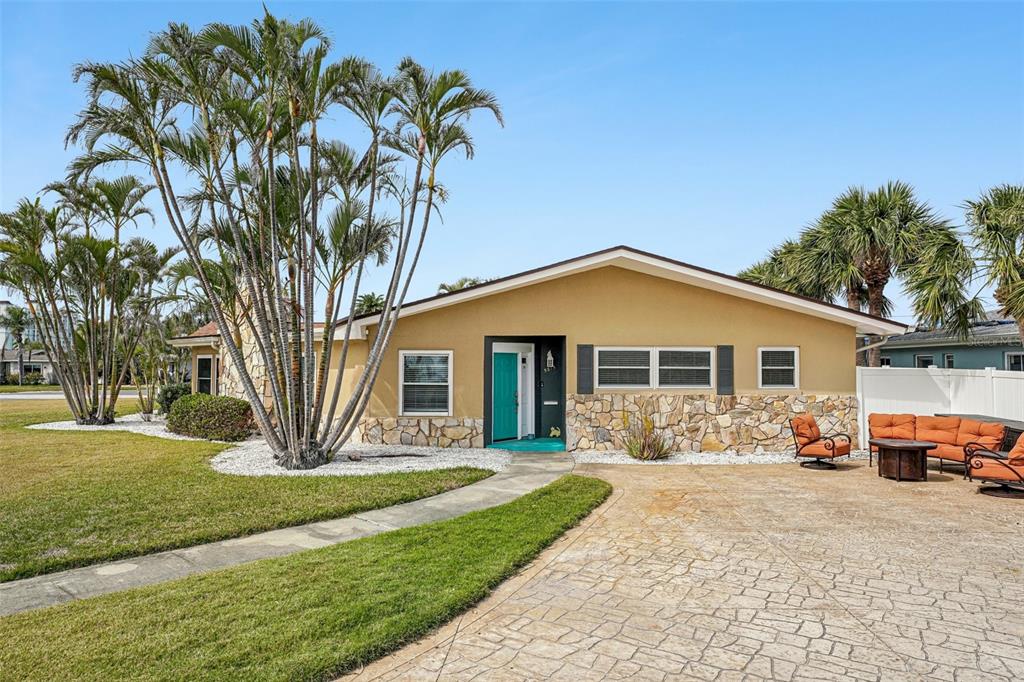 A single-story house with tan stucco, stone accents, and palm trees in the front yard — 5815 BALI WAY S, ST PETE BEACH, FL