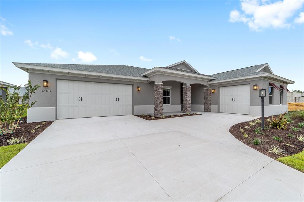 A single-story house features a gray stucco exterior, stone columns, and a three-car garage — 10305 SW 105TH TERRACE, OCALA, FL