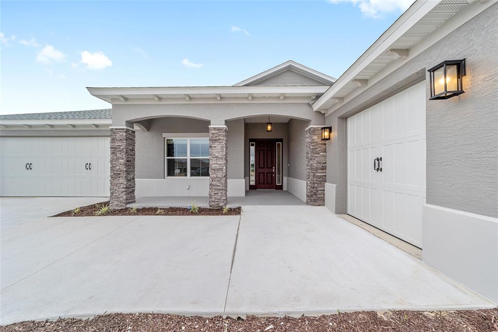 The exterior of a gray house features a covered porch, stone columns, and two garages — 10305 SW 105TH TERRACE, OCALA, FL