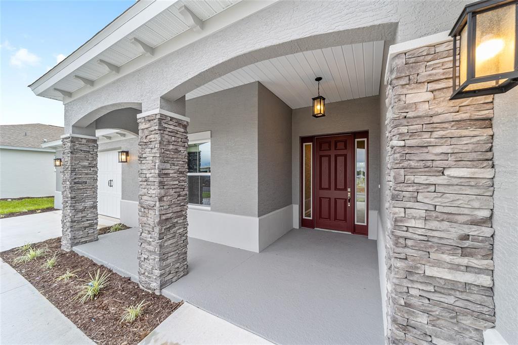 A covered front porch features stone-clad columns, a red front door, and gray stucco walls — 10305 SW 105TH TERRACE, OCALA, FL