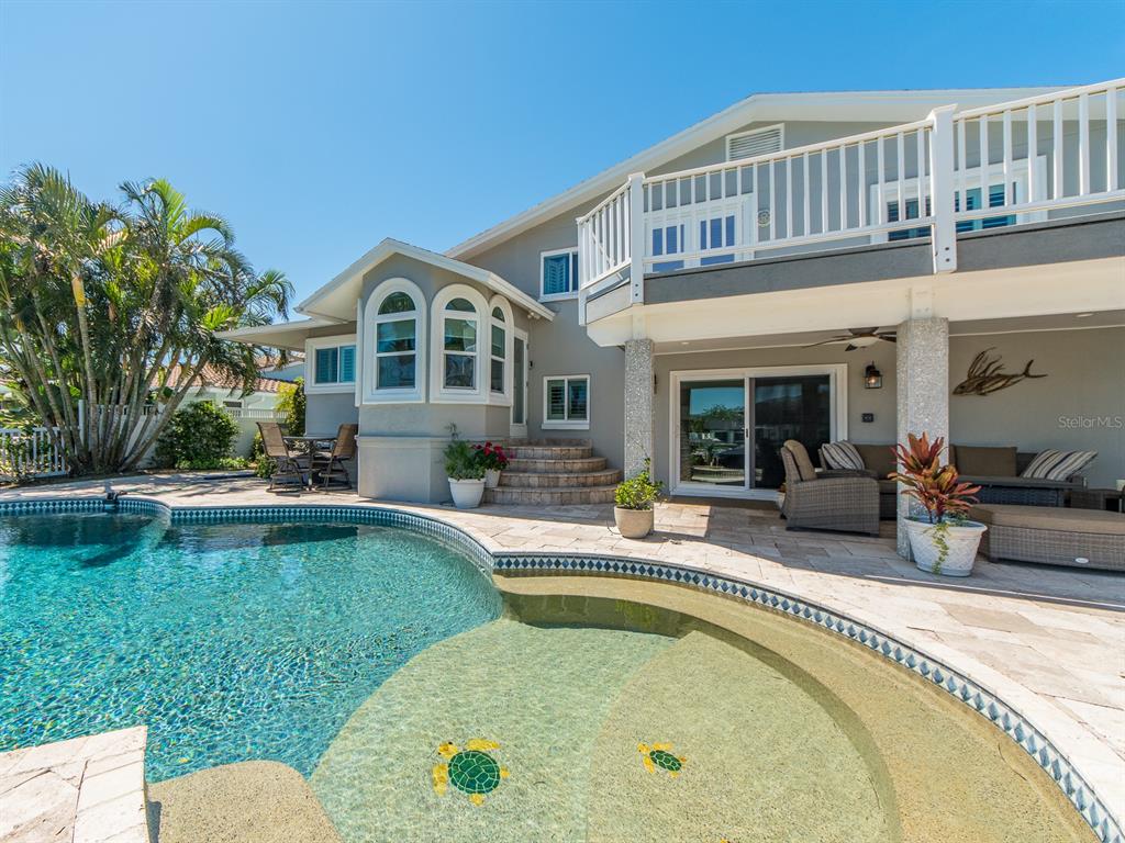 A two-story house exterior features a swimming pool with turtle mosaics and a covered patio — 707 SNUG ISLAND, CLEARWATER BEACH, FL