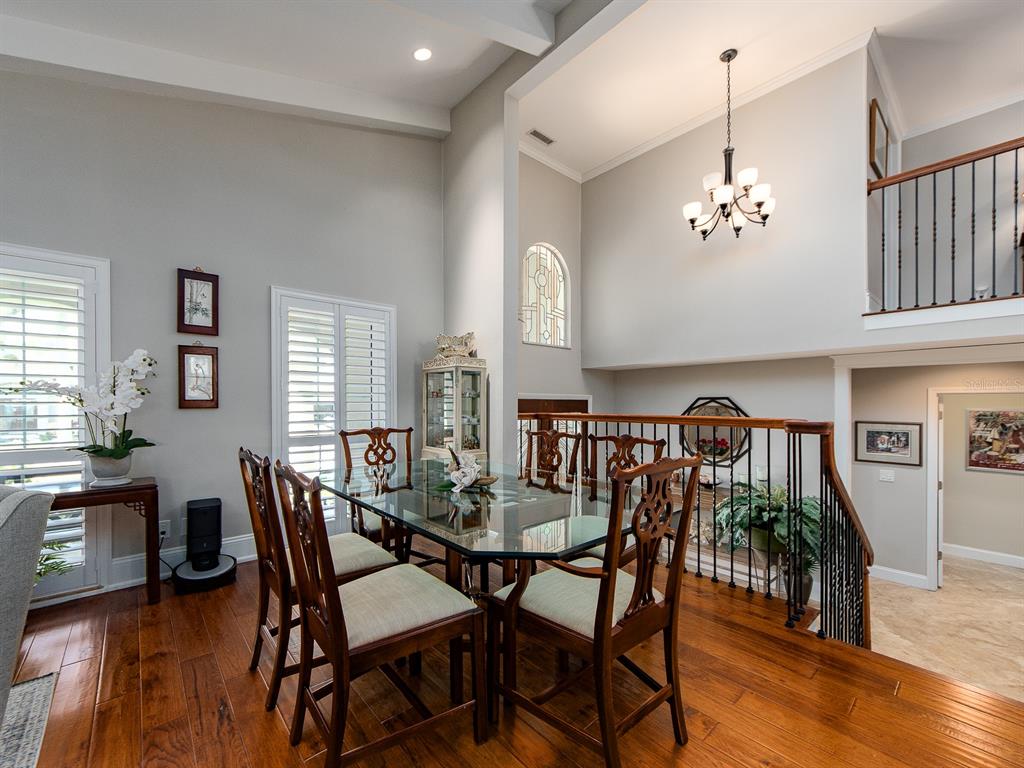 A dining area with a glass table, wooden chairs, hardwood floors, and a vaulted ceiling — 707 SNUG ISLAND, CLEARWATER BEACH, FL