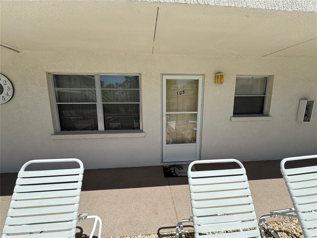A ground-level patio features three white lounge chairs, a screen door, and two windows — 510 GRANADA AVENUE UNIT 105, VENICE, FL