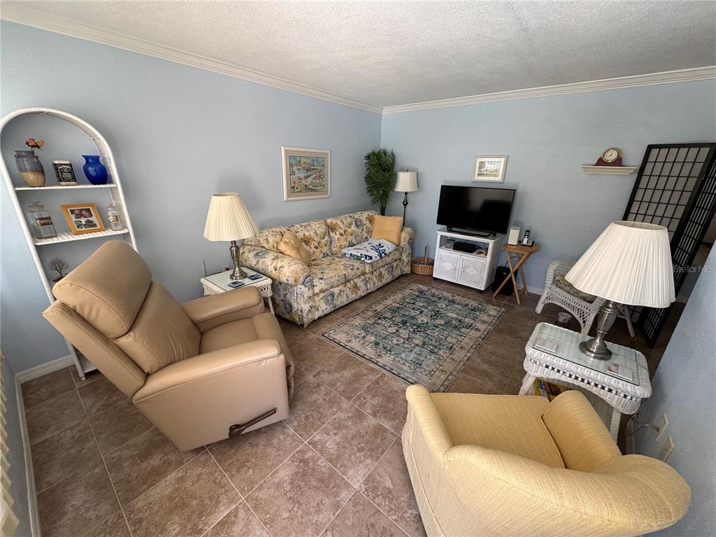 A living room features a floral sofa, a recliner, an armchair, and tile flooring — 510 GRANADA AVENUE UNIT 105, VENICE, FL