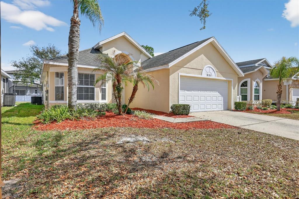 A single-story suburban house with a tan stucco exterior, a two-car garage, and palm trees — 931 EMERALD GREEN COURT, KISSIMMEE, FL