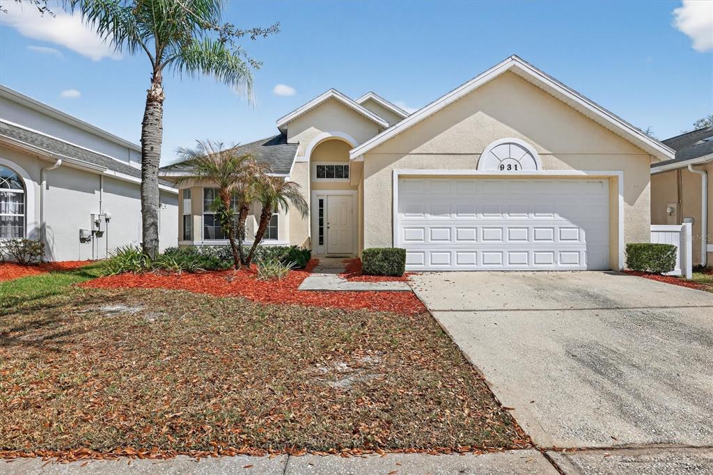 A single-story house with a beige stucco exterior, a two-car garage, and a palm tree — 931 EMERALD GREEN COURT, KISSIMMEE, FL