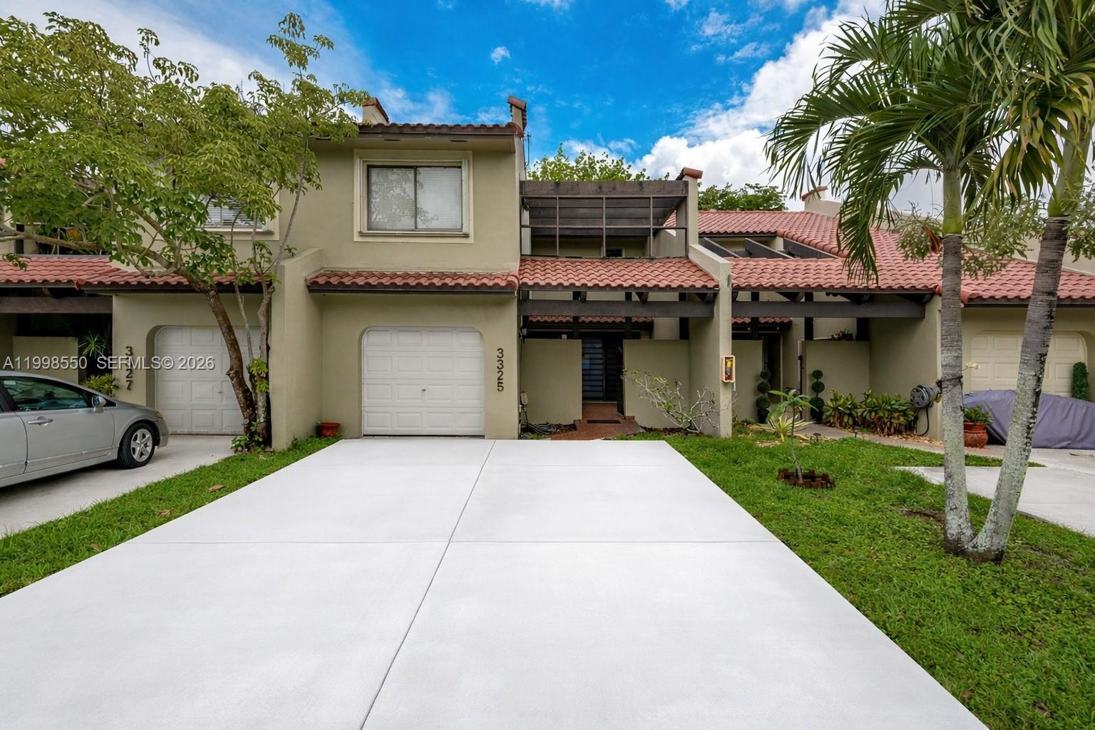 A two-story townhouse with a white garage door, a concrete driveway, and a tiled roof — 3325 Torremolinos Ave # 44, Doral FL 33178, DORAL, FL