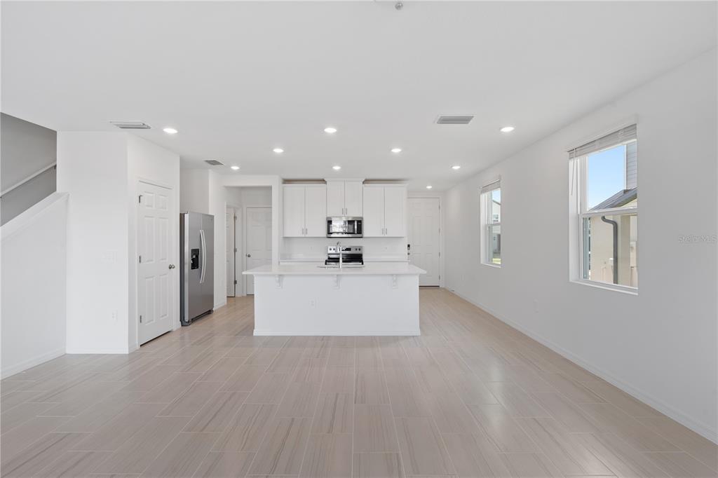 A bright, open-concept kitchen features white cabinetry, a central island, and light-colored tile flooring — 16452 HAPPY EAGLE DRIVE, CLERMONT, FL