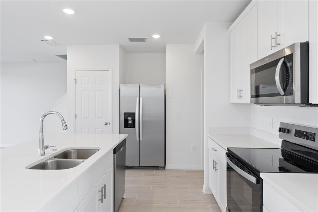 A modern kitchen features white cabinets, stainless steel appliances, an island with a sink, and tile flooring — 16452 HAPPY EAGLE DRIVE, CLERMONT, FL