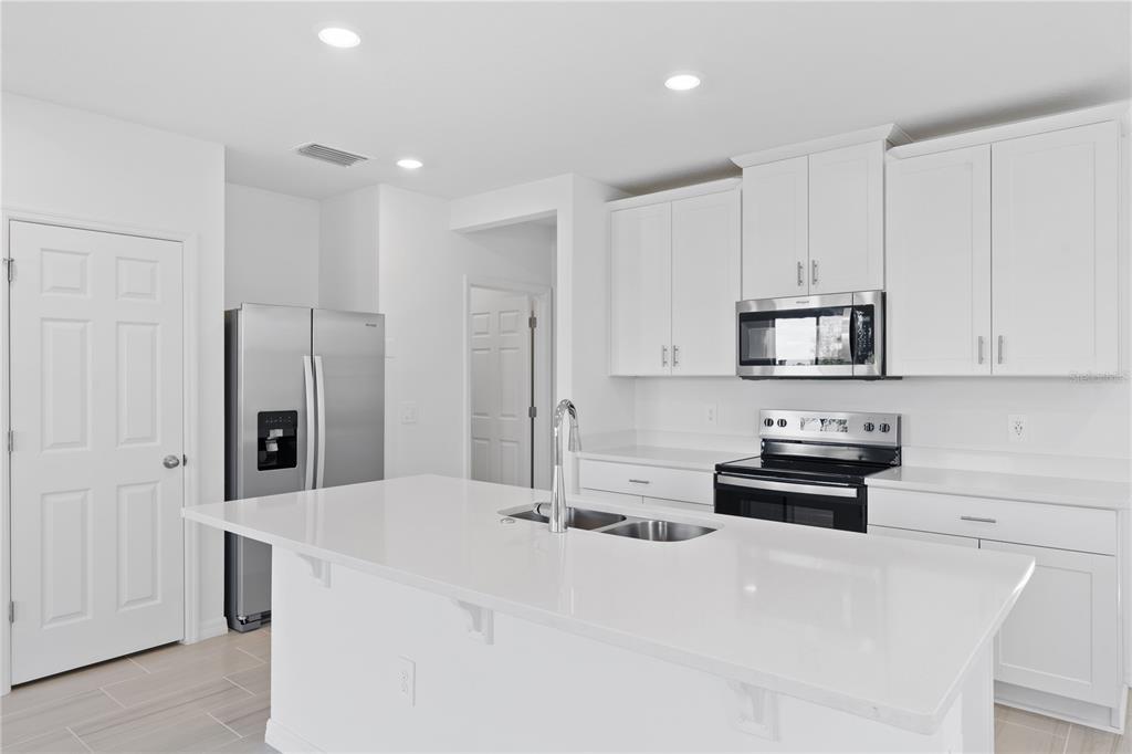 A modern kitchen features white cabinetry, stainless steel appliances, and a large central island — 16452 HAPPY EAGLE DRIVE, CLERMONT, FL