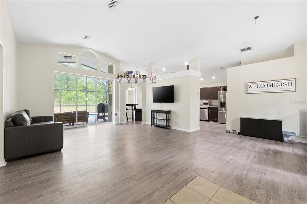 A spacious living room with light wood-look flooring, a sliding glass door, and an open kitchen — 11459 TRAIL RIDGE RUN, BROOKSVILLE, FL