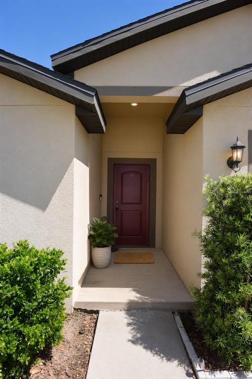A red front door is recessed under a covered entryway with a concrete walkway — 6936 CRESTED ORCHID DRIVE, BROOKSVILLE, FL