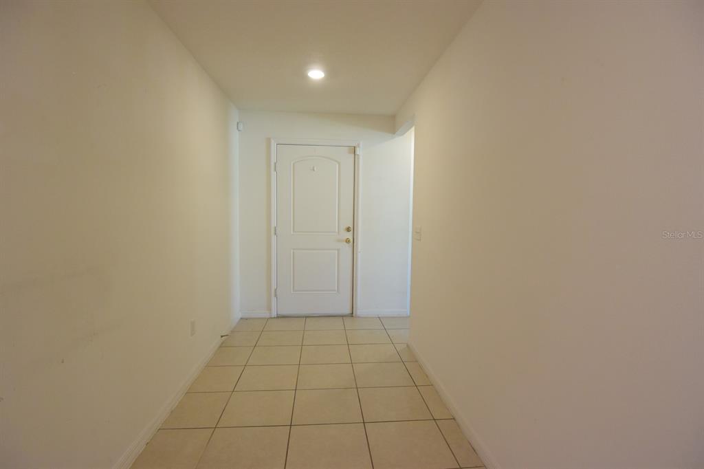 A hallway with beige tile flooring leads to a white front door — 6936 CRESTED ORCHID DRIVE, BROOKSVILLE, FL