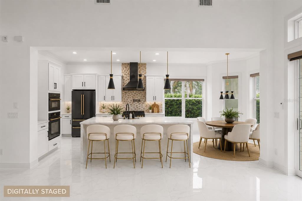A modern kitchen features white cabinetry, a marble island with gold stools, and dining area — 12664 BANTING TERRACE, ORLANDO, FL