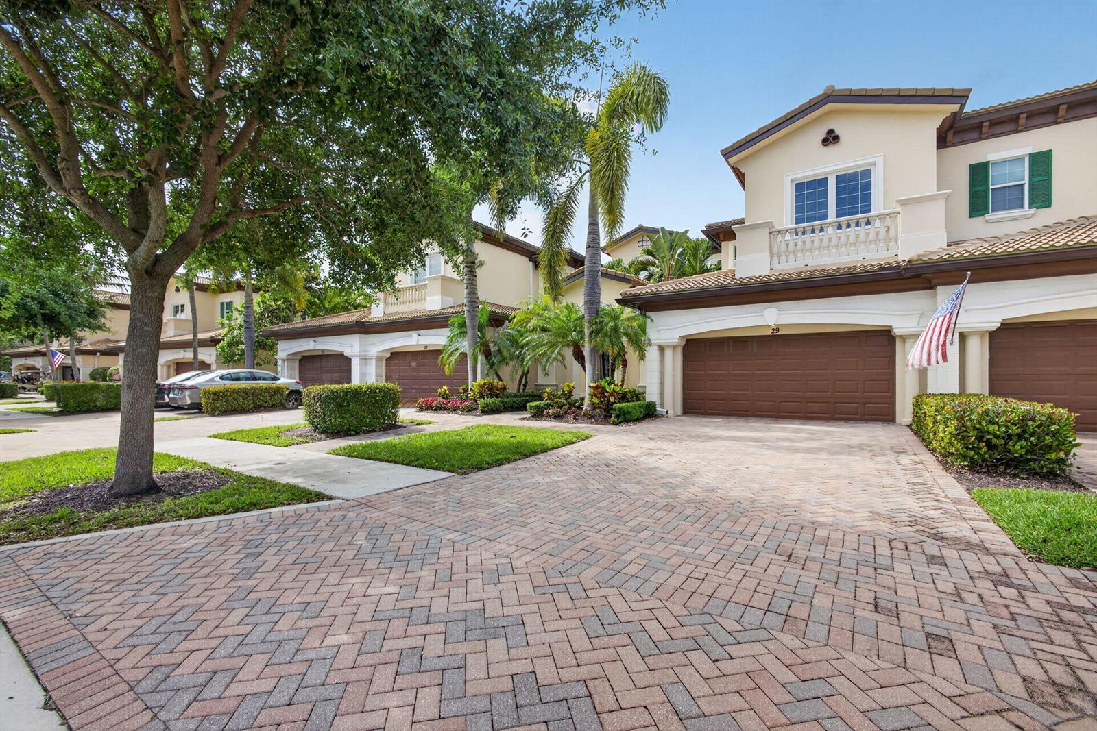 A paved driveway leads to the garage of a multi-story townhouse with palm trees — 111 Tresana Boulevard # 29, Jupiter FL 33478, JUPITER, FL