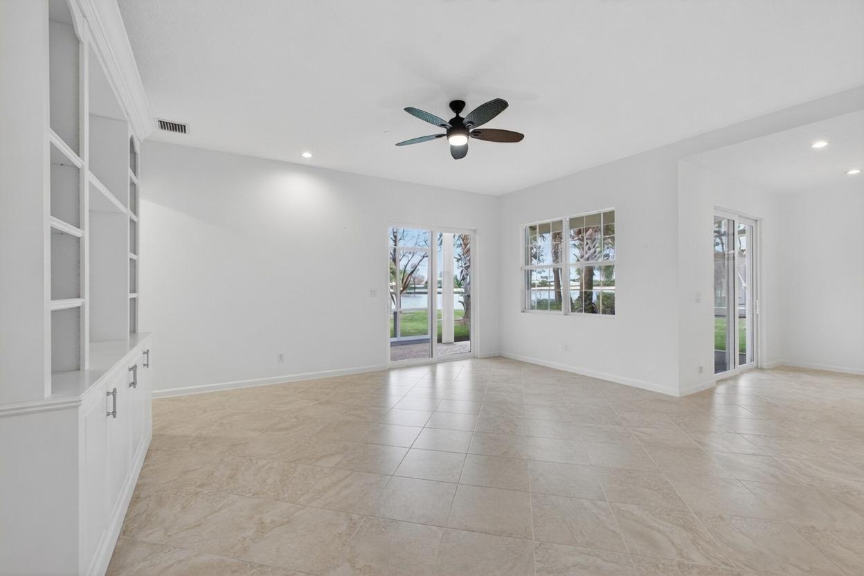 A bright, empty living room features white walls, tile flooring, built-in shelving, and ceiling fan — 111 Tresana Boulevard # 29, Jupiter FL 33478, JUPITER, FL