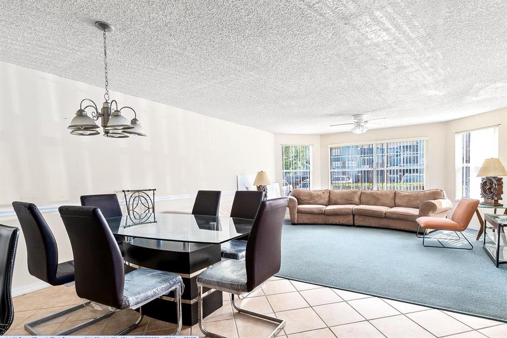 A dining area with a glass table and chairs transitions into a carpeted living room — 2741 N POINCIANA BOULEVARD UNIT 49, KISSIMMEE, FL