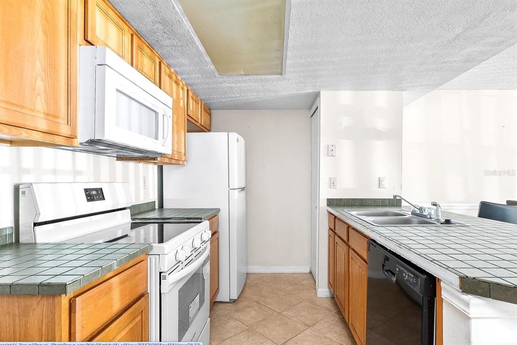 A kitchen with wood cabinets, white appliances, and tiled countertops — 2741 N POINCIANA BOULEVARD UNIT 49, KISSIMMEE, FL
