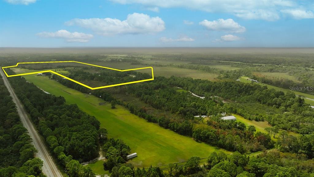 An aerial view shows a large, grassy field outlined in yellow next to a road — 520 HIGHLANDER DRIVE Lot 3, OAK HILL, FL