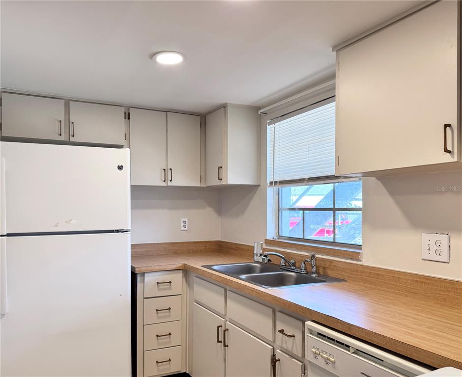 A kitchen features white cabinets, a white refrigerator, a double sink, and wood-look laminate countertops — 1000 S SEMORAN BOULEVARD UNIT 305, WINTER PARK, FL