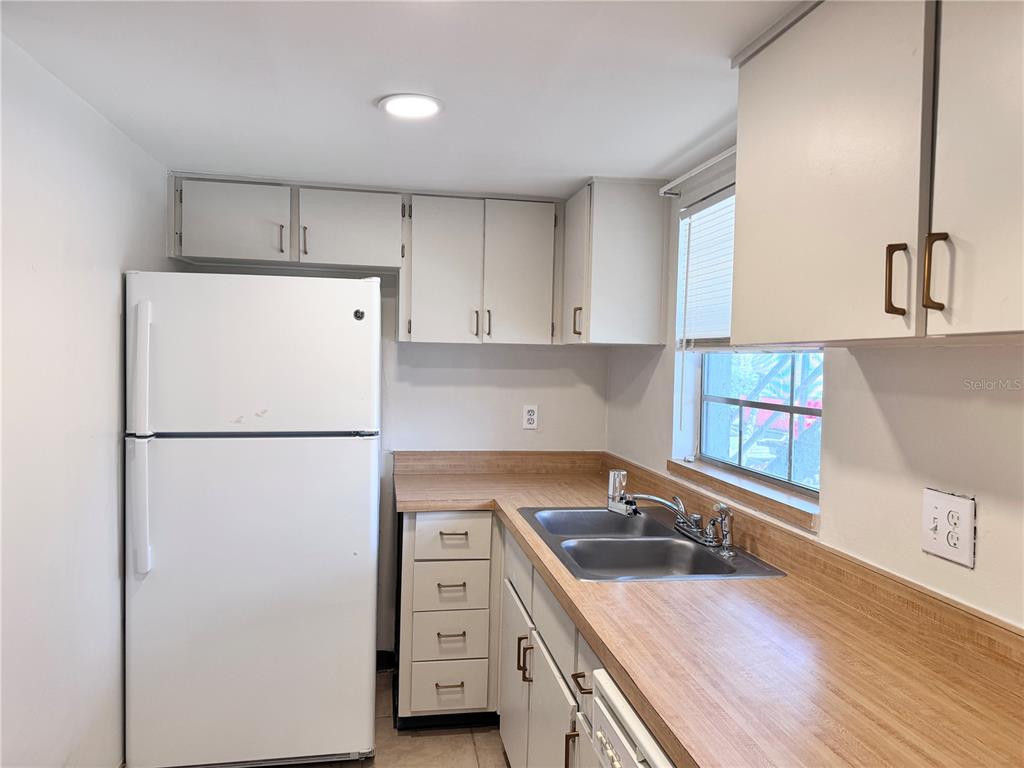 A kitchen features white cabinets, a white refrigerator, a double sink, and wood-look countertops — 1000 S SEMORAN BOULEVARD UNIT 305, WINTER PARK, FL