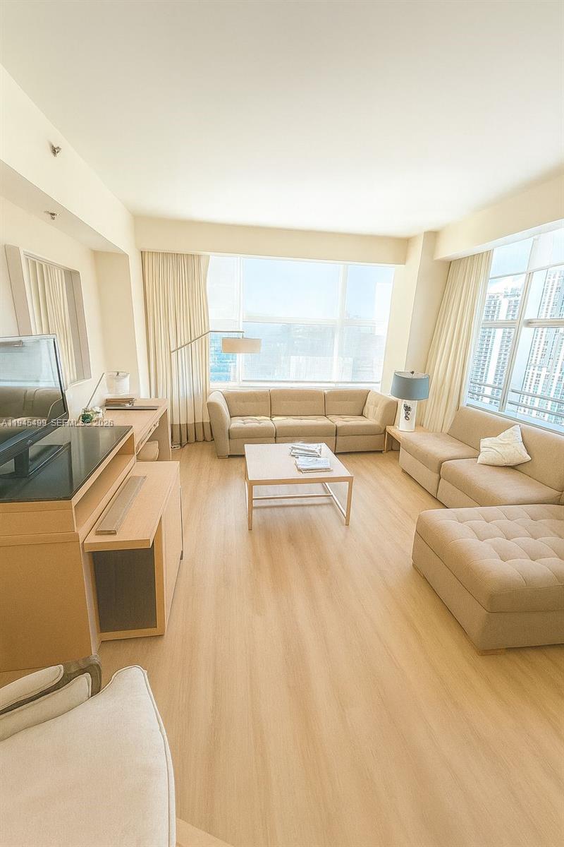 A living room features light wood flooring, a beige sectional sofa, and floor-to-ceiling windows — 1395 Brickell Ave # 2701, Miami FL 33131, MIAMI, FL