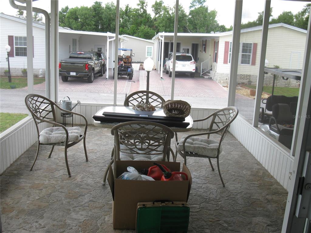 A screened-in porch features a dining set, stone-patterned flooring, and views of neighboring mobile homes — 242 RAMSGATE WAY, HAINES CITY, FL