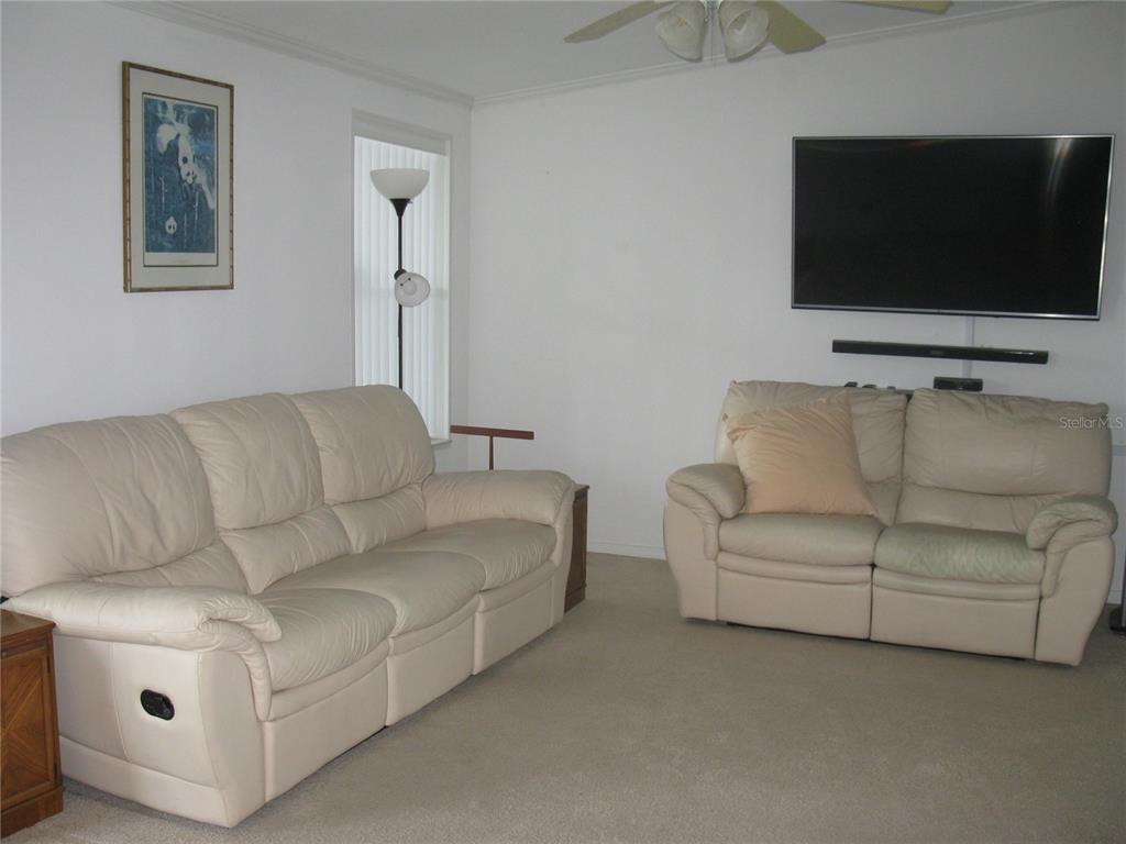 A living room features two cream-colored leather sofas, a wall-mounted television, and beige carpeting — 242 RAMSGATE WAY, HAINES CITY, FL
