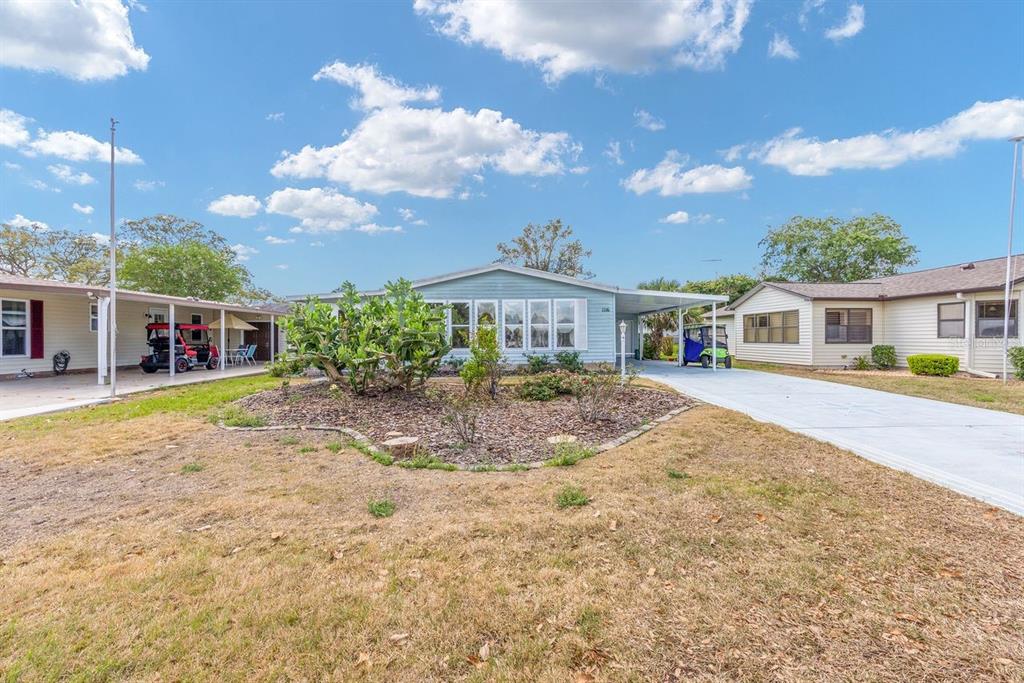 A light blue manufactured home with a carport and a landscaped front yard — 1116 W BOONE COURT, LADY LAKE, FL