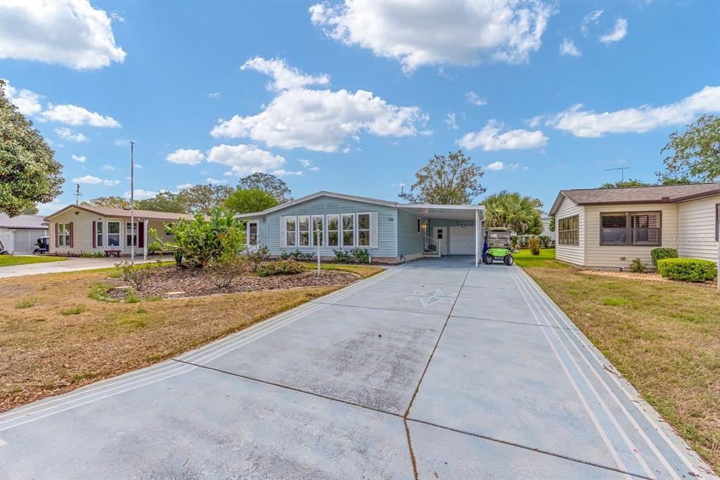 A light blue manufactured home features a concrete driveway, a carport, and a front yard — 1116 W BOONE COURT, LADY LAKE, FL