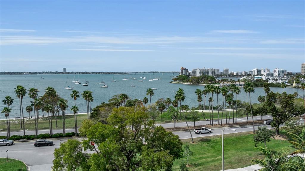 An elevated view of a bay with sailboats, a bridge, and coastal buildings beyond palm trees — 707 S GULFSTREAM AVENUE UNIT 802, SARASOTA, FL