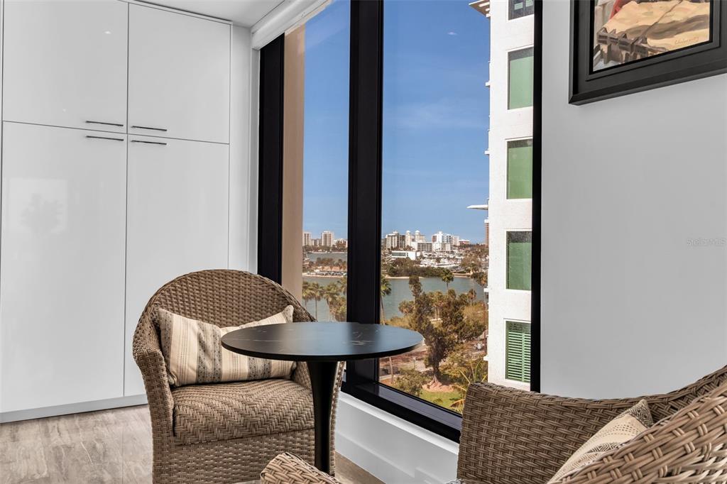 A seating area with two wicker chairs and a small table overlooks a coastal cityscape — 707 S GULFSTREAM AVENUE UNIT 802, SARASOTA, FL