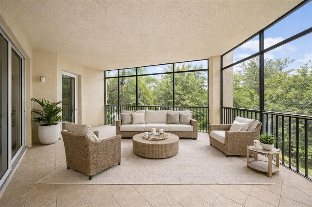 A screened-in patio features tiled floors, wicker furniture, and a view of lush green trees — 6482 WATERCREST WAY UNIT 204, LAKEWOOD RANCH, FL