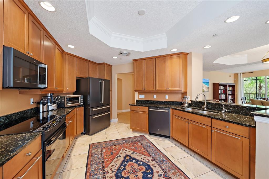 A kitchen features wood cabinets, dark granite countertops, stainless steel appliances, and a patterned area rug — 6482 WATERCREST WAY UNIT 204, LAKEWOOD RANCH, FL