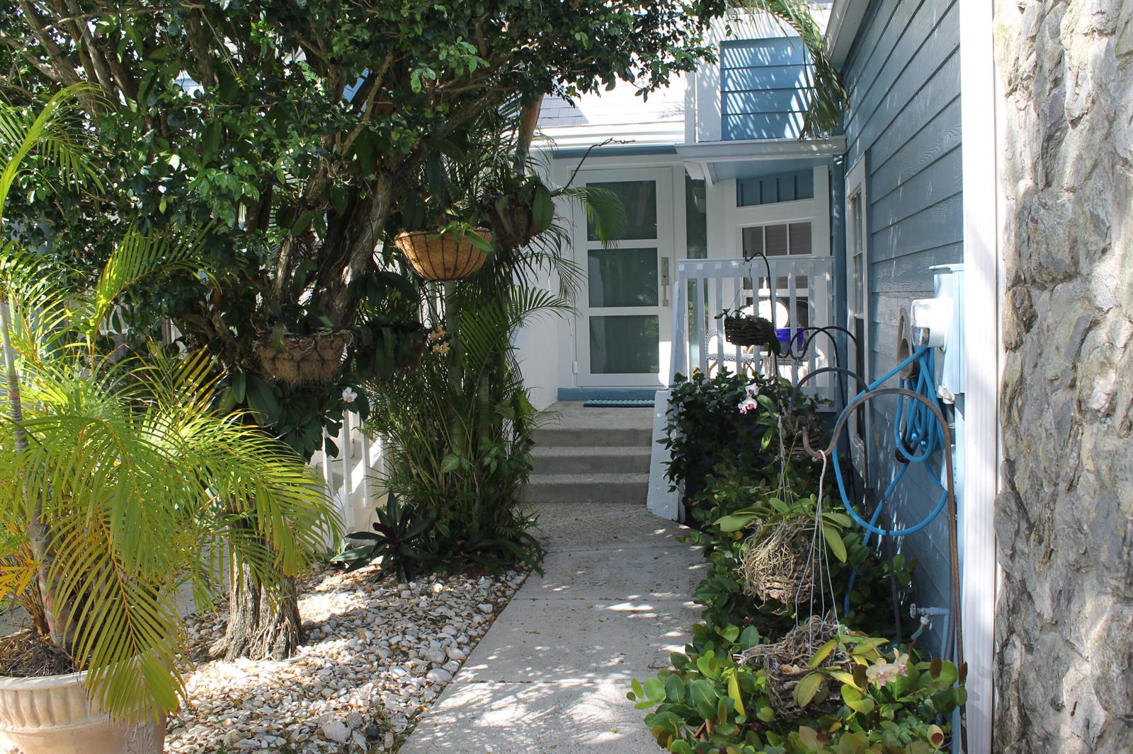 A concrete walkway leads to a white front door framed by lush tropical landscaping — 1120 Ocean Dunes Circle, Jupiter FL 33477, JUPITER, FL