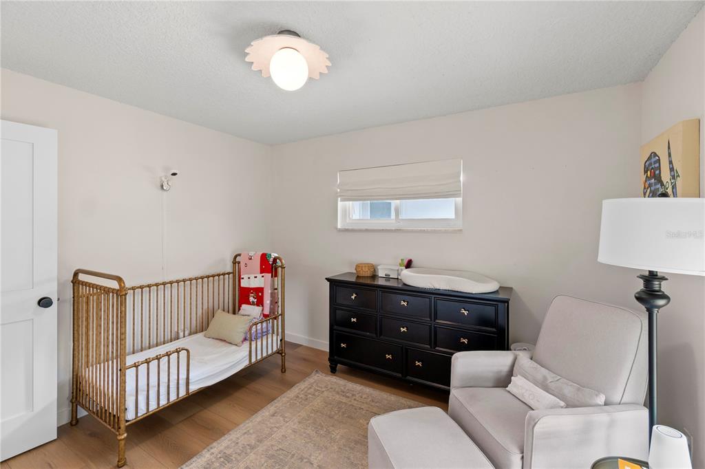 A nursery features a gold metal crib, a black dresser with a changing pad, and a chair — 5132 TELLSON PLACE, ORLANDO, FL