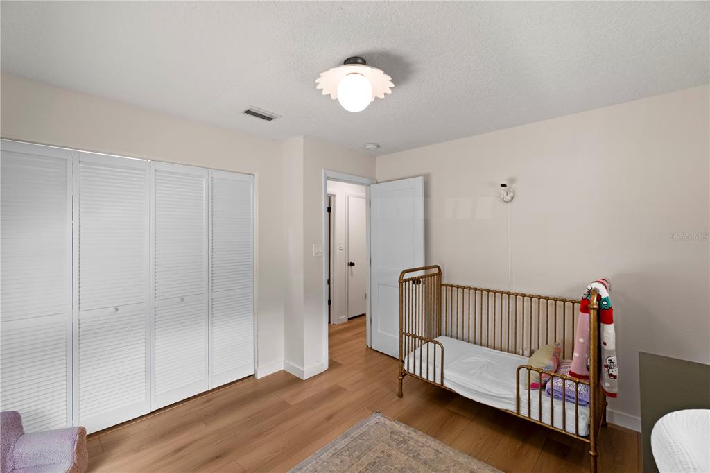 A bedroom features light wood flooring, a white louvered closet, and a gold metal crib — 5132 TELLSON PLACE, ORLANDO, FL