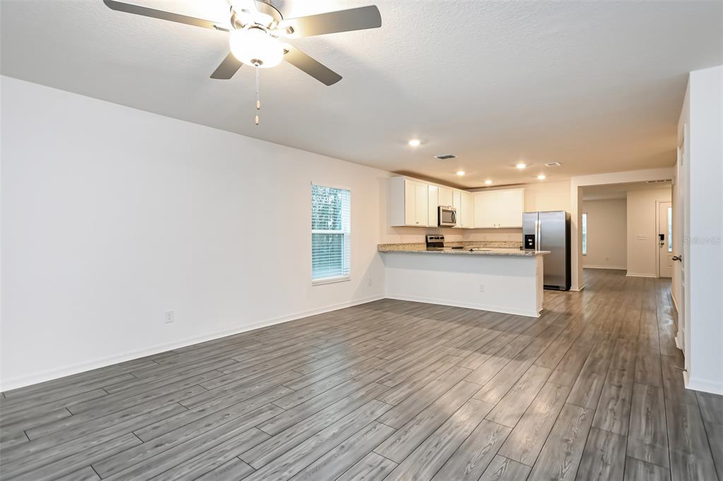 An open-concept living area features gray wood-look flooring, a ceiling fan, and a kitchen — 2006 MAPLE LANE, KISSIMMEE, FL