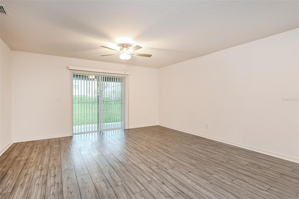 An empty room features light wood-look flooring, white walls, a ceiling fan, and sliding glass doors — 2006 MAPLE LANE, KISSIMMEE, FL