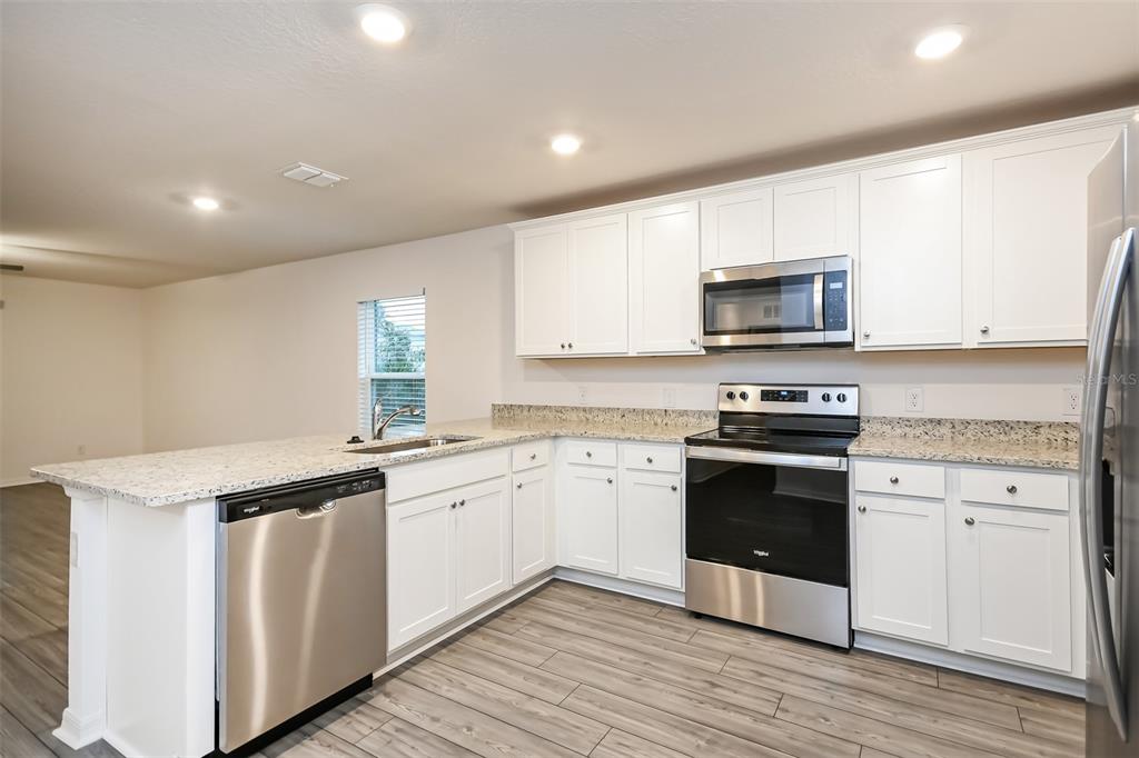 A kitchen with white cabinets, granite countertops, stainless steel appliances, and wood-look flooring — 2006 MAPLE LANE, KISSIMMEE, FL