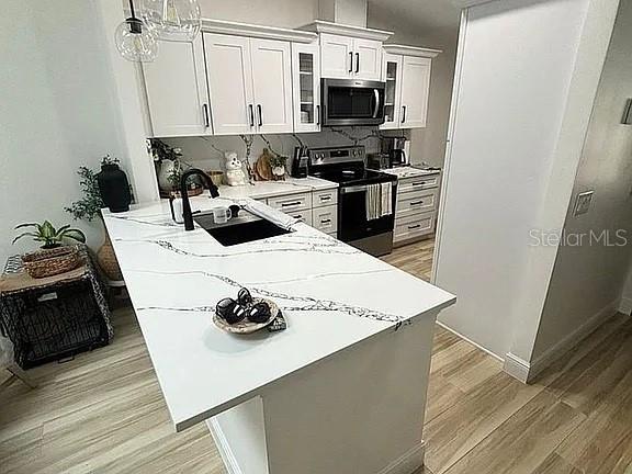 A kitchen features white cabinets, a marble-patterned island countertop, and light wood-look flooring — 1423A OAK PLACE, APOPKA, FL