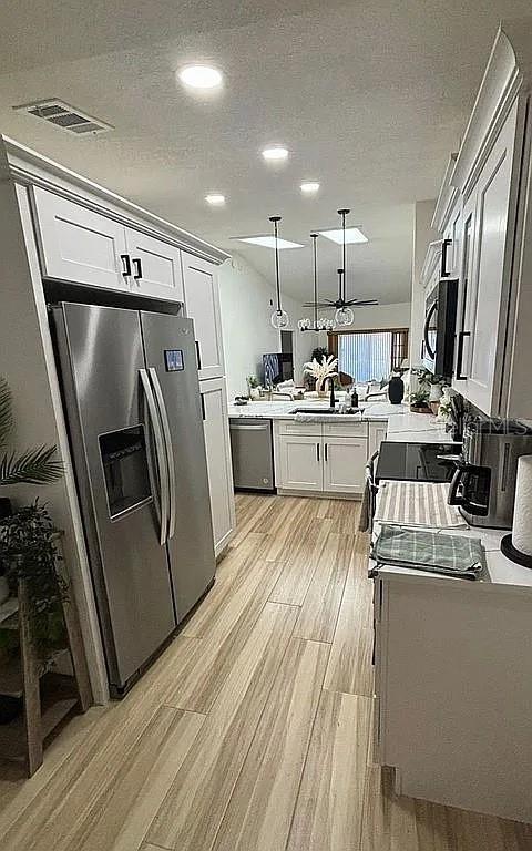 A modern kitchen features white cabinetry, stainless steel appliances, and light wood-look flooring — 1423A OAK PLACE, APOPKA, FL