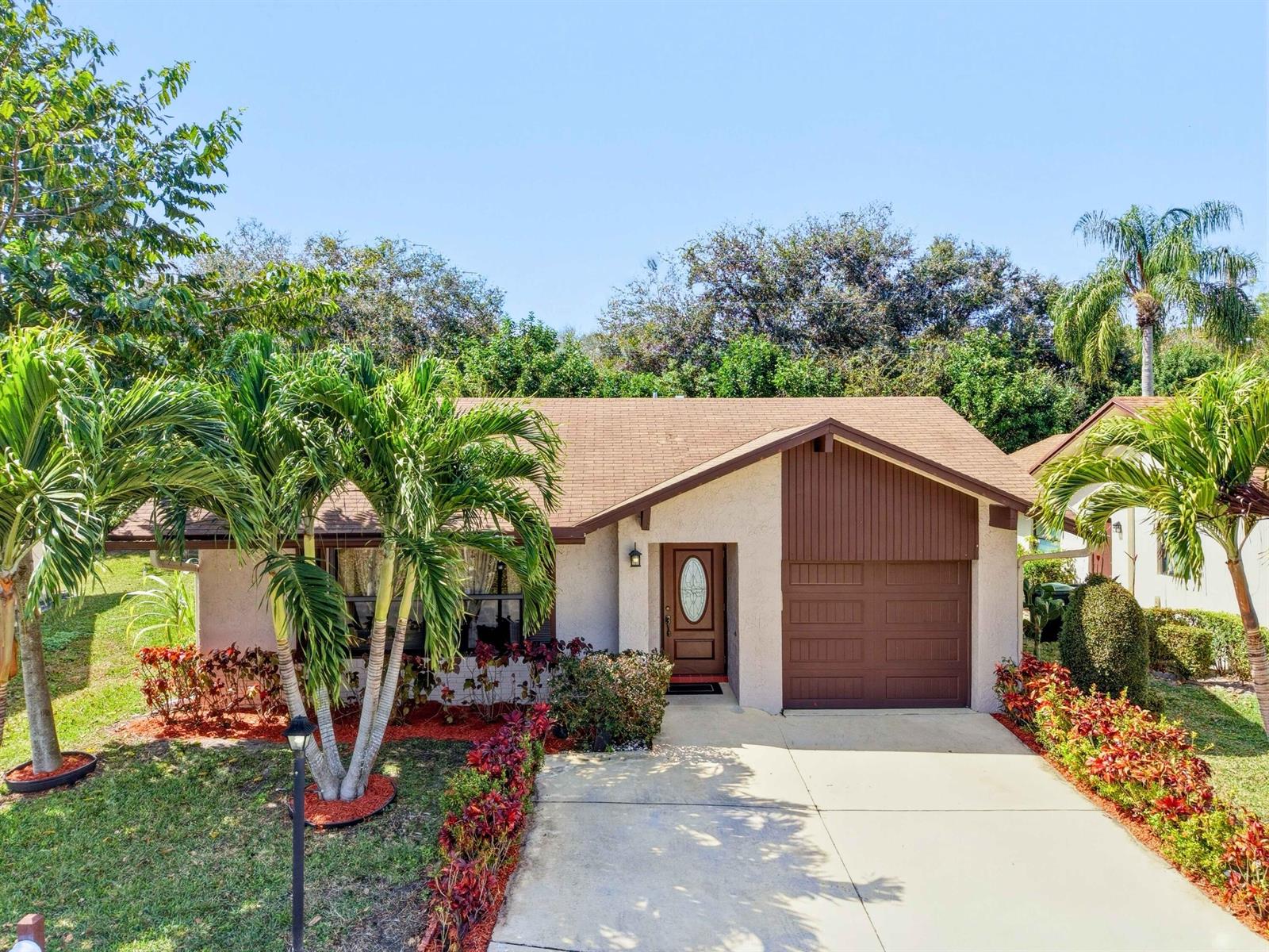 A single-story house with a brown roof, stucco exterior, and a front-facing garage — 6345 Tall Cypress Circle, FL 33463, FL