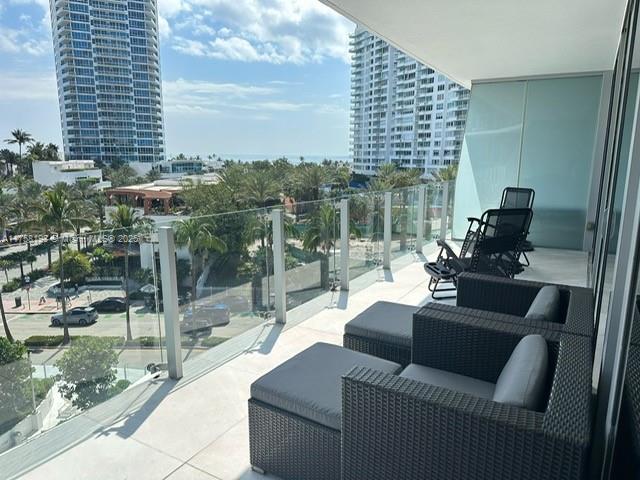 A balcony with dark wicker furniture overlooks a street, palm trees, and high-rise buildings — 1 Collins Ave # 602, Miami Beach FL 33139, MIAMI BEACH, FL