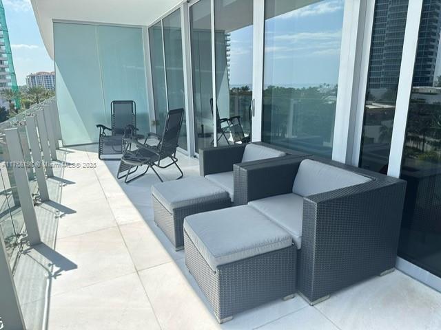 A balcony features outdoor wicker furniture, glass railings, and views of surrounding buildings — 1 Collins Ave # 602, Miami Beach FL 33139, MIAMI BEACH, FL