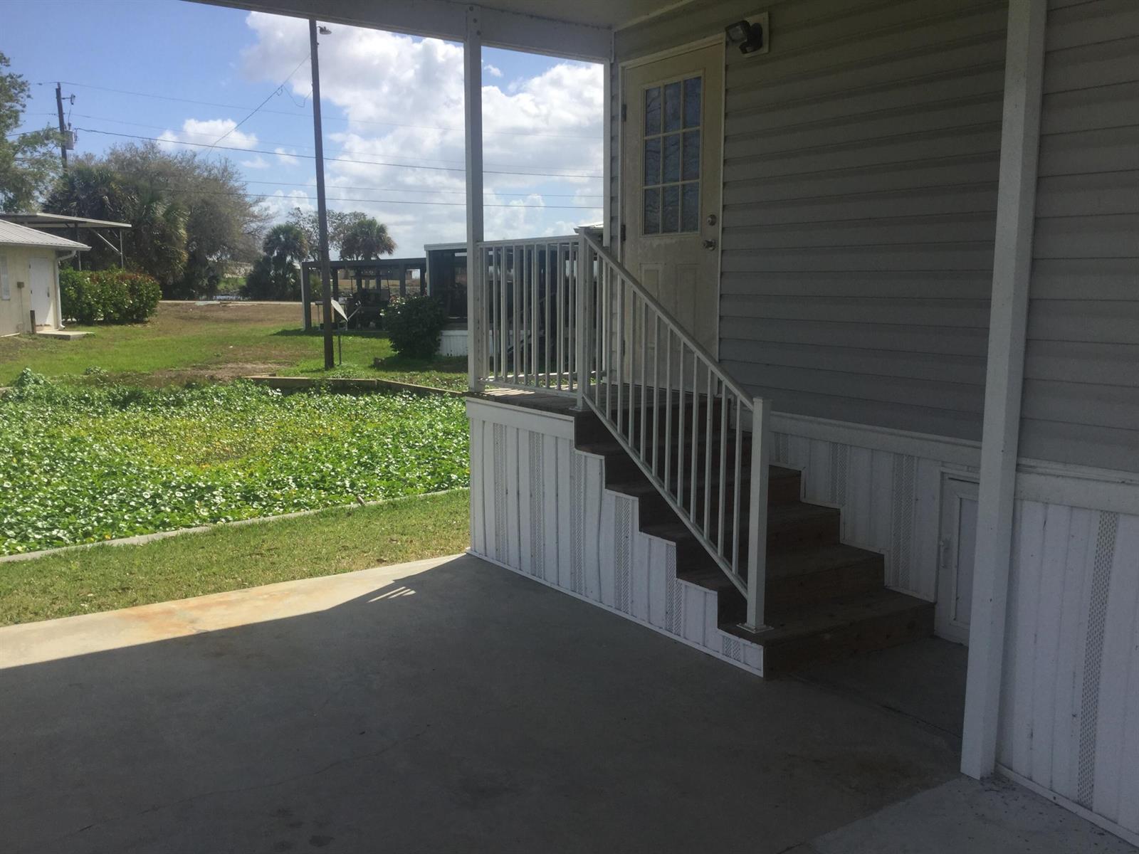 A concrete patio leads to a set of wooden stairs with a white metal railing — 1753 West Avenue, Moore Haven FL 33471, MOORE HAVEN, FL