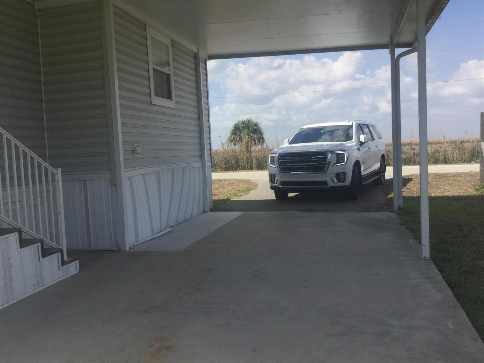 A white GMC SUV is parked under a carport next to a light-colored mobile home — 1753 West Avenue, Moore Haven FL 33471, MOORE HAVEN, FL