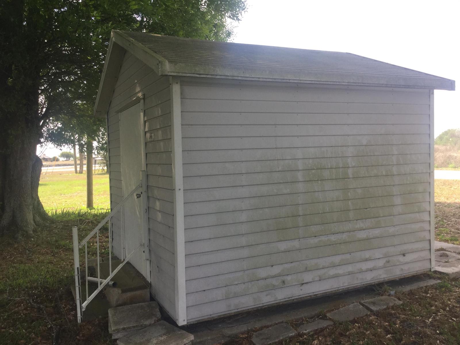 A small, light-colored storage shed with a single door and metal railing stands outdoors — 1753 West Avenue, Moore Haven FL 33471, MOORE HAVEN, FL
